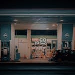 A nighttime view of a gas station and convenience store with a car parked at the pump.